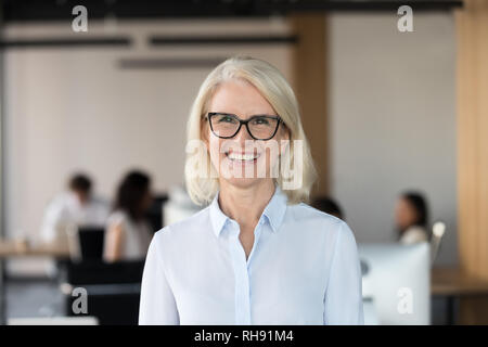 Freundliche senior Geschäftsfrau in Gläsern bei Kamera schaut im Büro Stockfoto