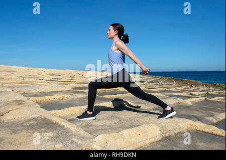 Frau tut eine Schulter, stretch, Warm-up Übungen draußen in der Sonne auf den Maltesischen Salinen Stockfoto