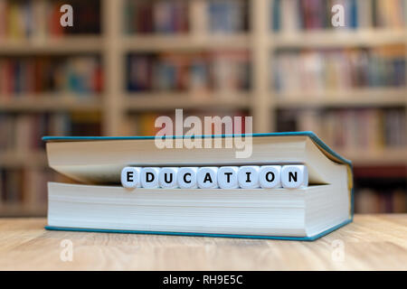 Würfel in Buchform das Wort 'Bildung'. Buch liegt auf einem hölzernen Tisch in einer Bibliothek. Stockfoto