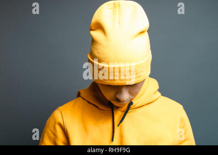 Porträt der jungen Rapper mit gelber Mütze Mütze und Kapuze, vor grauem Hintergrund Stockfoto