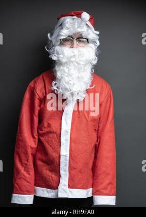 Portrait der unbeholfenen Santa Claus mit übergroßen Kostüm vor grauem Hintergrund Stockfoto