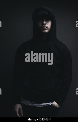 Junge coole Rapper mit schwarzem Kapuzenpullover und Kappe vor grauem Hintergrund Stockfoto