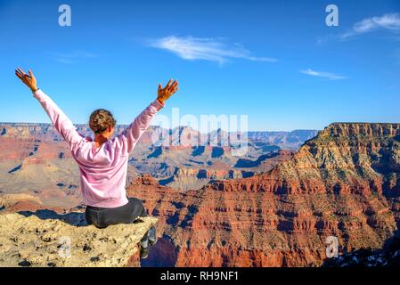 Junge Frau in die Ferne suchen, gerne mit ausgestreckten Armen, am Abgrund der gigantischen Schlucht des Grand sitzen Stockfoto