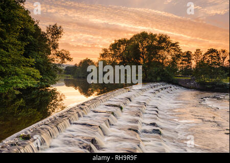 Einen malerischen Sonnenuntergang Himmel über ländliche Landschaft (Wasser sanft fließende Wehr Schritte) - River Wharfe, Burley in Bösingen, Yorkshire, England, UK. Stockfoto