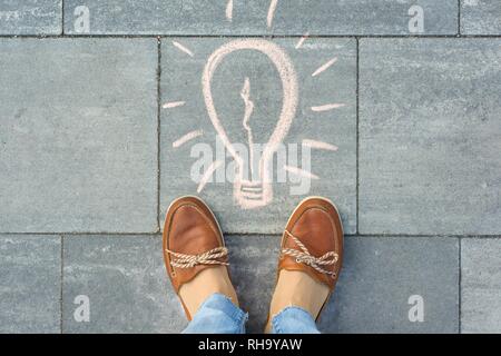 Weibliche Füße mit abstrakten Bild Zeichnung des Lichts blulb ongray Bürgersteig geschrieben Stockfoto