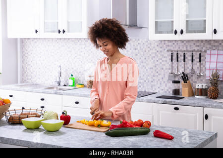 Junge Glücklich afrikanische Frau Schneiden gelbe Paprika auf Schneidebrett in der Küche Stockfoto