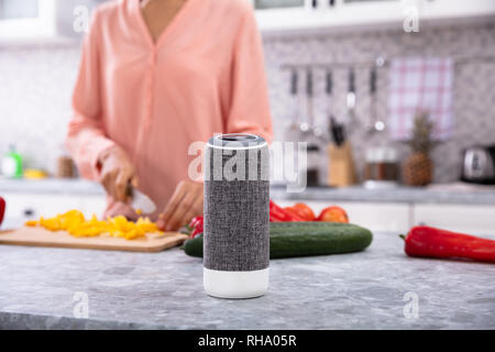 Nahaufnahme einer Frau, die das Arbeiten in der Küche mit Smart Lautsprecher vorne Stockfoto