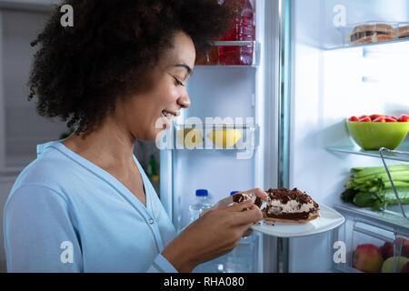 Nahaufnahme einer Frau, die in der Nähe von offenen Kühlschrank Essen das Stück Kuchen Stockfoto