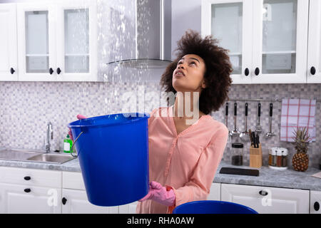 Nahaufnahme einer Sorgen junge Frau Sammeln von Wasser von der Decke in die Blaue Schaufel Stockfoto