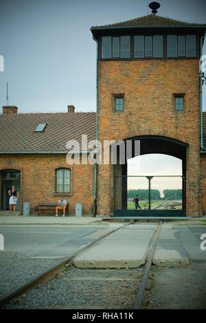 Von der Haupteinfahrt in Birkenau (Auschwitz II - Birkenau) aus führt eine Eisenbahnlinie mit Touristen, die draußen rauchen. Stockfoto