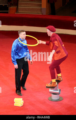 Frohe clown amüsant Publikum im Zirkus Arena. Clown macht gute Laune. Clown auf roten Zirkus arena Kleider Hoop für Künstler Stockfoto