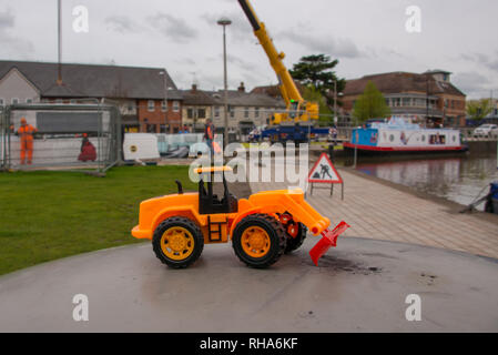 Lustiges Spielzeug Bulldozer mit echten Bau und Ausrüstung im Hintergrund Stockfoto
