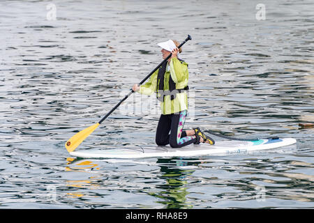 Vancouver, Kanada - 23 September 2017: aktive kaukasische erwachsene Frau Mitte 30 kniend auf paddle Board auf dem Fluss tragen grüne Regenmantel und Schirmmütze Stockfoto