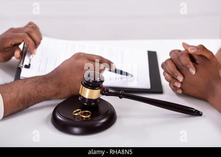 Nahaufnahme von einem Richter erklären Vertrag zu seinen Klienten mit Hammer und Goldene Ringe Stockfoto
