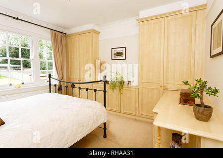 Modernes Schlafzimmer mit neutralen Farben, Gusseisen Doppelbett und Einbauschränken Stockfoto