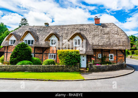 Ein traditionelles englisches Landhaus mit Strohdach. Brick House mit grünen Bäumen, auf der Seite der Straße. Kleine, rustikale Haus in Chawton. Sommer holid Stockfoto