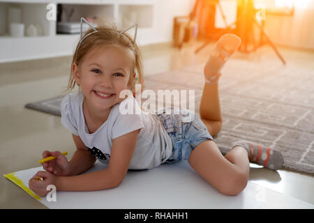 Glückliches Kind. Foto betrachten Seite kreative Mädchen liegen in der Nähe der Bücher und Spielwaren, Zeichnen Stockfoto