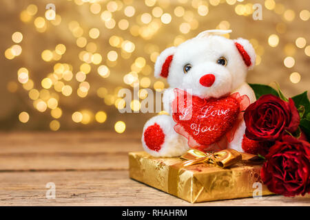 Valentines Tag Konzept. Weiß Plüsch Spielzeug tragen, rote Rosen und Geschenkbox, auf hölzernen Tafel mit Kopie Platz für Text. Selektive konzentrieren. Stockfoto