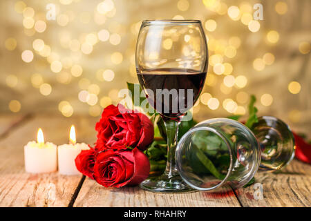 Valentinstag noch leben. Zwei Gläser Wein, rote Rosen und brennende Kerzen auf einem rustikalen Holztisch vor einem hellen Hintergrund verschwommen. Stockfoto