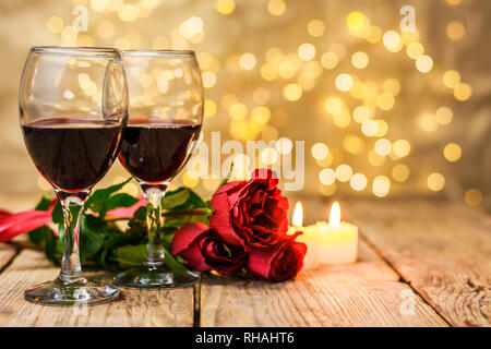 Valentinstag Konzept. Zwei Gläser Wein, rote Rosen und brennende Kerzen auf einem rustikalen Holztisch vor einem unscharfen Hintergrund leuchtend mit Co Stockfoto