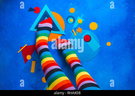 Mädchen Beine in Regenbogen gestreifte Socken auf einen farbigen Hintergrund mit Colour-blocking einfache Formen. Abstrakte Geometrie flach Stockfoto