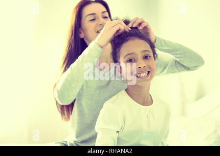 Fröhliches kleines Mädchen erhalten ihr Haar durch ihre fürsorgliche Mutter. Stockfoto