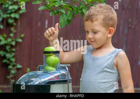 Junge Kind macht Saft aus grünen Äpfel im Entsafter im Freien. Stockfoto