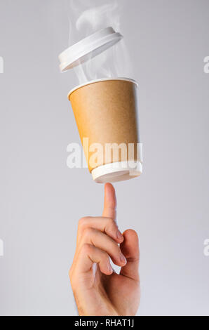 Eine Tasse mit heißem Kaffee und eine Wolke von Dampf Salden auf der Fingerspitze. Frei schwebende Schale aus Kunststoff Deckel. Kaffeepause Konzept. Leeren platz für Stockfoto