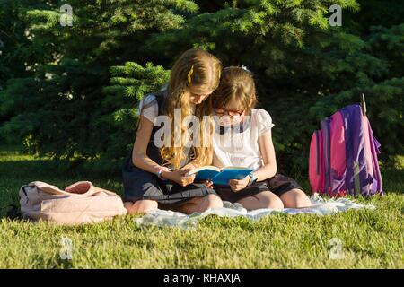 Zwei kleine Mädchen Freunde Schülerin lernt sitzen auf einer Wiese im Park. Kinder mit Rucksäcken, Bücher, Notebooks Stockfoto