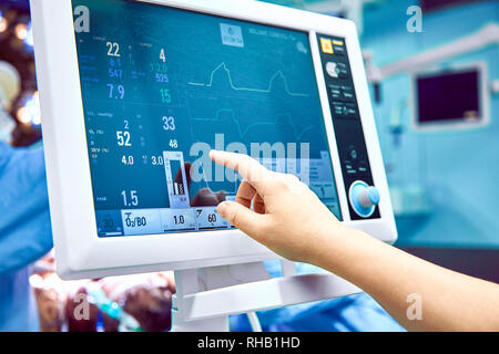 Die Überwachung der Vitalparameter des Patienten im Operationssaal. Arzt bei der Vitalparameter des Patienten cheking. Elektrokardiogramm Monitor während der Operation in Betrieb. Stockfoto