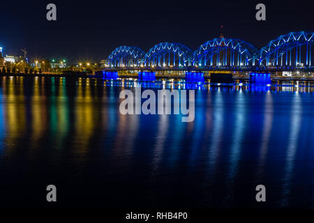 Eisenbahn Brücke überquert den Fluss Daugava in Riga bei Nacht. Panoramablick auf die Lettische Hauptstadt Riga Stadt vom linken Ufer der Daugava. Stockfoto