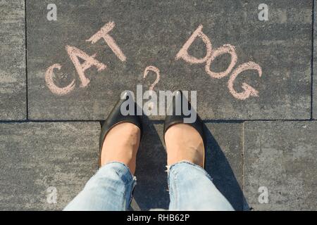 Frau vor der Wahl Katze oder Hund. Ansicht von oben, weibliche Füße mit Text Katze Hund auf grau Bürgersteig geschrieben Stockfoto