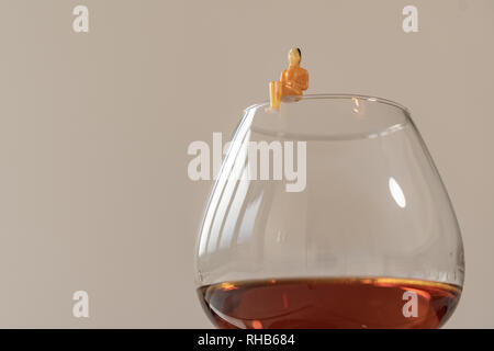Miniatur Frau Abbildung des Standorts auf dem Glas Brandy. Flache Tiefenschärfe Hintergrund. Healthcare und Alkoholismus Konzept. Stockfoto