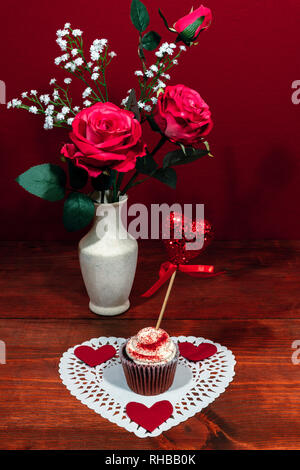 Schöne rosa Rosen in einer Vase mit Baby's Atem Blumen, herzförmige Weisse dollie mit einem Becher Kuchen mit einem Herz auf einen Pick akzentuiert. Stockfoto