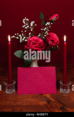 Schöne rosa Rosen in einer Vase mit Baby's Atem Blumen akzentuierte, zwei lit ed Kerzen in Crystal Halter und einer Karte Stockfoto