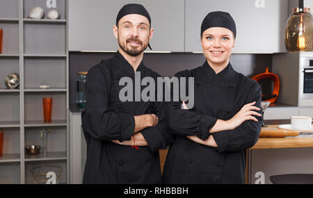 Porträt von zwei zuversichtlich persönliche Köche in der modernen Inneneinrichtung der privaten Küche stehend Stockfoto