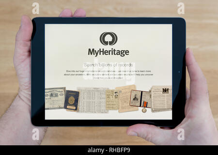 Ein Mann schaut auf die MyHeritage Website auf seinem iPad tablet device, Schuß gegen einen hölzernen Tisch top Hintergrund (nur redaktionelle Nutzung). Stockfoto