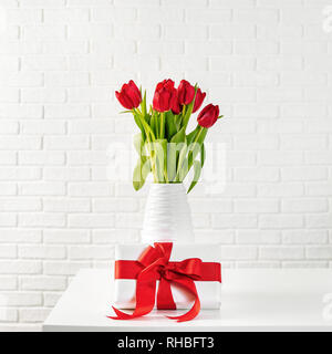 Platz geschossen von roten Tulpen in weißen Vase mit Geschenk mit roter Schleife Stockfoto