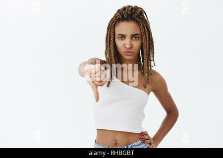 Portrait von Missfallen ernst - auf der Suche Attraktive afrikanische amerikanische Frau mit gelben Dreads grinsend aus Abneigung, Daumen nach unten in die missbilligung Stockfoto