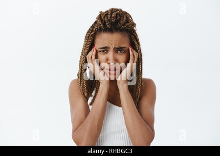 Taille-up Shot von Betroffenen und perplex miserabel dunkelhäutige Frau mit Dreadlocks runzelte die Stirn berühren Tempel versuchen konzentrieren Gefühl Kopfschmerzen Stockfoto