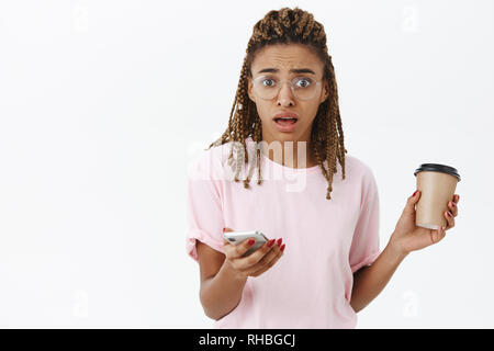 Taille- schuss besorgt und ängstlich niedlichen afrikanische amerikanische Frau mit dreads in Frames, Rosa t-shirt, die eine neue Tasse Kaffee und Smartphone Stockfoto