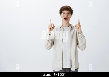 Enthusiastisch und charismatische gut aussehende junge Mann mit lockigem Haar in runde Gläser und Shirt überrascht und glücklich wie die Hände und Stockfoto