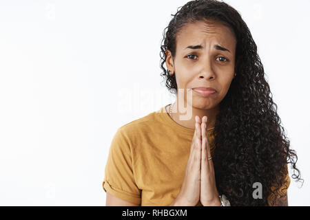 Bitte ich brauche Sie. Portrait von Jammern dumm und traurige Junge niedlich african-american Girl mit Langen lockigen Haare, Hände halten, beten, weinen und Grimassen Stockfoto