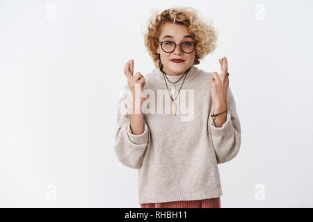 Gut aussehende aufgeregt charmante europäische weiblich in 20 s mit Haar in Gläsern und Pullover lächelte hoffnungsvoll, begeistert die Daumen für gutes Glück als Stockfoto