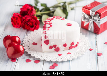 Marzipan weiß Kuchen in der Form eines Herzens mit roten Herzen. Als Dekoration Strauß roter Rosen Ein Geschenk der Band. Hochzeit oder Valentinstag Stockfoto