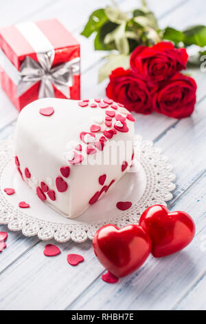 Marzipan weiß Kuchen in der Form eines Herzens mit roten Herzen. Als Dekoration Strauß roter Rosen Ein Geschenk der Band. Hochzeit oder Valentinstag Stockfoto