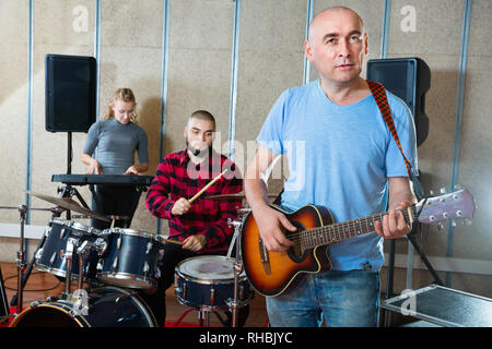 Probe von Music Group. Fröhliche positive Band Leader Gitarre spielen und singen mit seinen Musikern im Studio Stockfoto