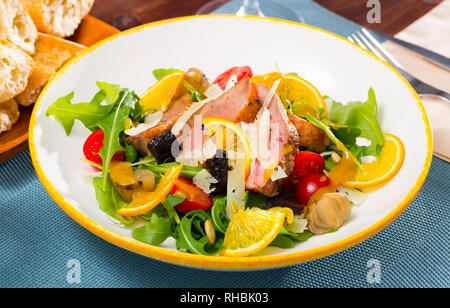 Bunter Salat von Ente Filets mit frischem Rucola, Tomaten, Zwiebeln, in Scheiben Parmesan, Trockenpflaumen und orange Stockfoto