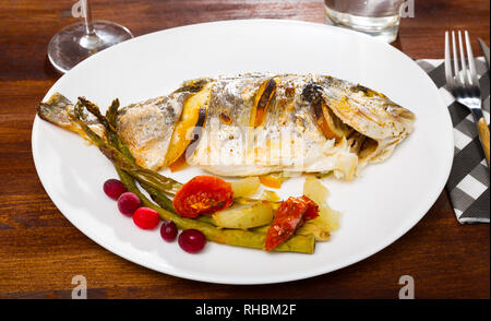 Dorade im Ofen gebacken serviert mit Spargel, Zwiebeln und Tomaten Stockfoto