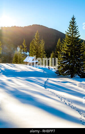 Schnee weg, der zu einer hölzernen Hütte in die Berge führt. Die Fichten sind mit morgen Strahlen behandelt. Rauch aus dem Kamin der h Stockfoto